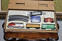 Full view of train set pieces in original molded plastic tray inside box, showing train cars, track, and power supply.
