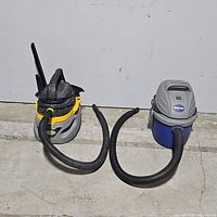 Both vacuum cleaners side by side against white background, showing hoses, handles, and bodies.