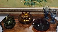 Lot of vintage glassware including green glass bowls, amber glass flower bowl, ruby red bowl, amber plates, and blue sundae glasses.