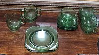 Group photo showing the pitcher, two-handled mug, five standard mugs, and two saucers in signature green depression glass.