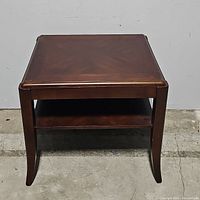 Front view of walnut brown side table with one shelf, showing shape and curvature of legs.
