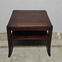 Front view of the walnut brown side table showing rectangular top, curved legs, and lower shelf.