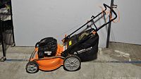 Side view of the orange and black Yard Force EX675 gas lawn mower with collection bag attached and push handle extended.
