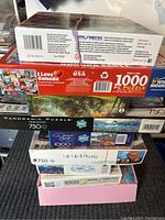 Stack of nine boxed puzzles showing various titles and piece counts, including 750 and 1000 pieces.