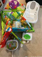 Lot of baby items including colorful activity gym, white baby bathtub, multiple toys, and baby monitor.