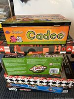 Stack of six board games including Cranium Cadoo, Watermelon Smash, Smash Game, Star Wars Monopoly, and two others with partially visible titles