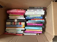 Top-down view of assorted book lot in a cardboard box, showing titles and condition.