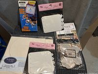 Lot of various craft items displayed on black surface including Fiskars embossing system, Build-A-Book kits, Technique Tiles, and papers