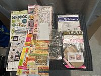 Lot of assorted craft items including scrapbook refills, cardstock stickers, clear stamps, and embellishments spread on table