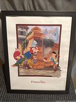 Full view of the Disney Pinocchio framed print showing colorful characters and village scene within black frame.