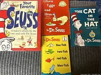 Four Dr. Seuss books laid out on a carpeted floor showing front covers: Your Favorite Seuss (red cover), Green Eggs and Ham (red cover), One Fish Two Fish Red Fish Blue Fish (yellow cover), and The Cat in the Hat (blue cover).