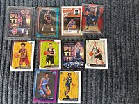 Photo showing all 10 NBA rookie basketball cards arranged on dark carpet, featuring multiple players and series with varied styles and finishes.