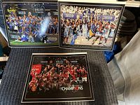 Full view of all three framed English Premier League championship celebration prints placed on a carpeted floor, showing the Manchester United, Chelsea, and Manchester City teams with trophies.