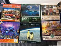 Lot of 6 various 1000-piece puzzles showing covers with different nature and scenic themes.