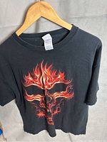 Front view of black vintage T-shirt with fiery skull print hung on wooden hanger