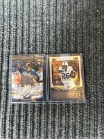 Two sports rookie cards side by side on carpet background. Left card is Ronald Acuna Jr. baseball card in top protective sleeve, right card is Saquon Barkley rookie football card in bottom protective sleeve.
