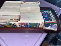 Photo of over 200 sports trading cards arranged in stacks inside a wooden tray, showing primarily the backs of the cards with some visible fronts portraying athletes, mostly from football, baseball, and basketball.