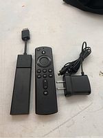 Photo showing Amazon Fire Stick device, remote control, and USB power adapter with cable on a flat surface