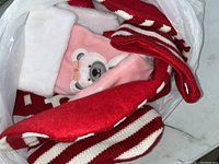 Photo showing a plastic bag containing multiple Christmas holiday stockings. A red and white striped stocking, a pink stocking with bear embroidery, and a white cuff stocking are visible.