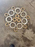 Top-down photo of large round metal circle wall decor on concrete floor showing multiple smaller circular mosaic insets with missing glass in one