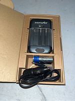 Image of Digipower universal battery charger in cardboard packaging box, accompanied by a power cord and rechargeable battery.