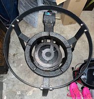 Top view of a black metal gas stove burner with circular burner surrounded by metal frame and stand legs.