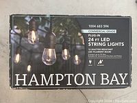 Box showing Hampton Bay commercial grade 24 ft LED string lights with 12 shatter resistant LED filament bulb sockets.