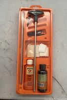 Photo of Hoppes Gun Cleaning Tool Kit in orange plastic tray showing cleaning rod, cleaning patches, and bottles of Hoppe's lubricating oil and solvent.