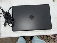 Closed HP laptop showing top cover with HP logo and attached power cord.