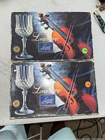 Two original boxes of Longchamp vintage crystal wine glasses with branding and violin artwork on the top, showing the boxes are unopened and in original condition.