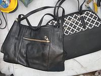 Two purses: one black leather with gold zipper on the front, the other black and white patterned purse with black handles.