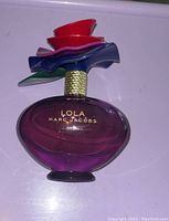 Photo showing Marc Jacobs Lola perfume bottle with colorful flower-shaped cap and purple gradient bottle.