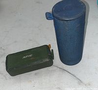 Blue cylindrical Ultimate Ears speaker and green rectangular Apie speaker on white surface