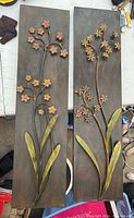 Photo of two vertical metal wall decor panels with floral designs including stems, yellow flowers and green leaves.