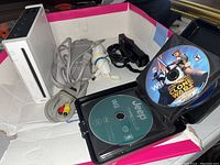 White Nintendo Wii console with power and AV cables, two Wii remotes, and an open game case showing multiple Wii game discs including Star Wars: The Clone Wars and Jeep Thrills.