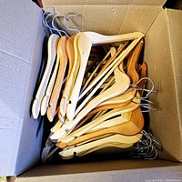 Box filled with wooden clothes hangers in light to darker wood finishes with metal hooks, showing quantity and condition.
