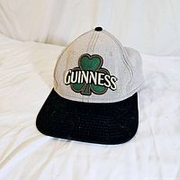 Front view of grey and black Guinness baseball cap with green shamrock and white text embroidered on front