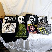 Folded black T-shirts with various horror and sci-fi graphics including 'I'd Rather Be Undead', a large eyeball, a green Creature from the Black Lagoon, a screaming face, Eraserhead, and The Brain Eater.