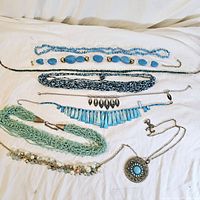 Full view of vintage costume jewelry lot displayed on white fabric background showing various blue and turquoise necklaces with diverse materials and designs.