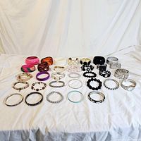 Overview of all bracelets, bangles, and the watch laid out on white fabric, showing variety in color and material