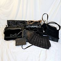 Photo showing the entire lot of black vintage purses and bags in varying sizes and styles arranged on a white fabric background.