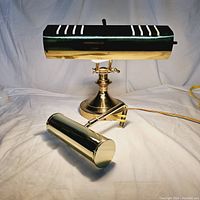 Banker piano lamp and wall mounted brass lamp shown together on a white background, highlighting the brass finish and overall design.