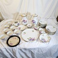 Wide view showing the set's cups, teapots, serving platter, bowls, and plates all decorated with pink and purple anemone flowers and gold accents.