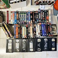 Photo showing a large assortment of VHS tapes arranged with their jackets and tapes visible. Titles include Home Alone, Beetlejuice, Back to the Future, Wayne's World, Lord of the Rings, and many others.