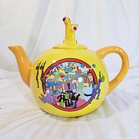 Full front and side view of yellow ceramic teapot showing handle, spout and front artwork