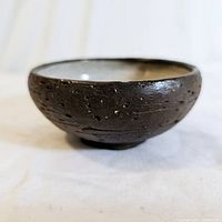 Side view of small dark brown textured ceramic bowl on white background
