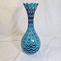 Front view of the tall blue and white hand-blown art glass vase, showing scalloped rim and blue wavy pattern on bulbous body.
