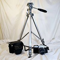 Overall view showing the tripod fully extended, the camera with lens and case on the surface in front, highlighting the included items and condition of tripod.