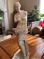 Front and side view of 19-inch lightweight porcelain Venus de Milo statue placed on a wooden table with natural lighting in room surroundings.