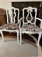 Pair of painted white dining/accent chairs, one with arms, both with patterned upholstered seats, standing on carpet in front of fireplace.